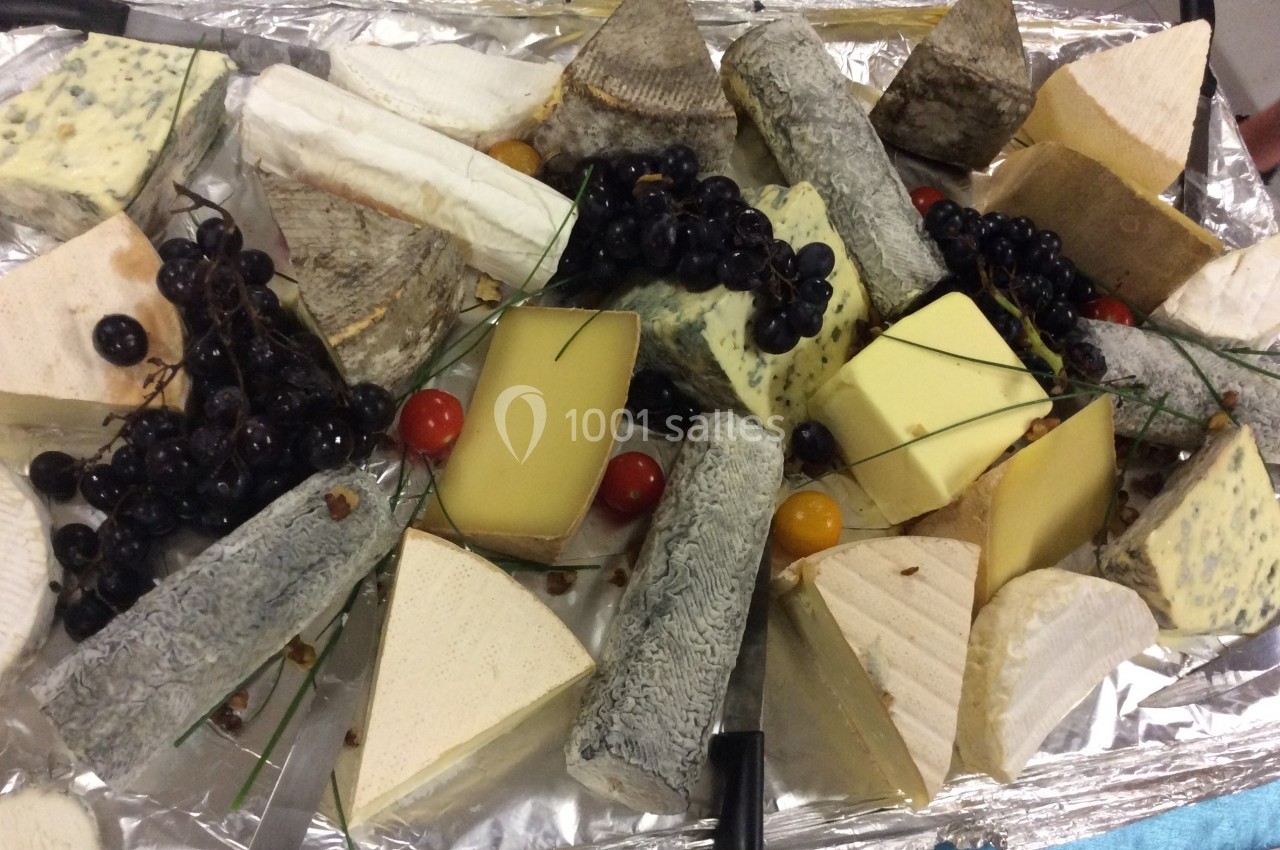 Plateau varié de fromages artisanaux avec raisins noirs, tomates cerises et brins de ciboulette sur un fond argenté.