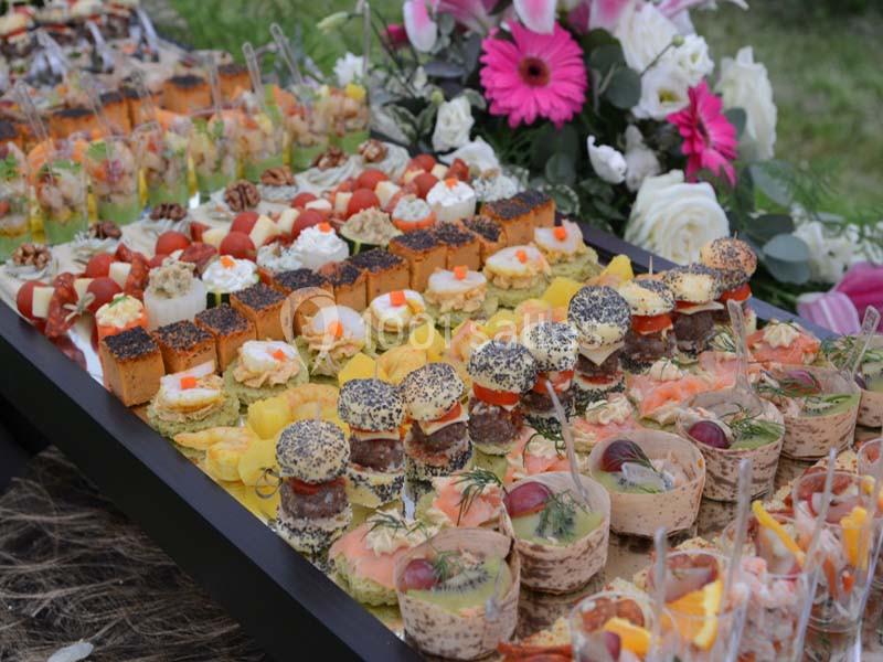 Plateau de canapés variés avec fleurs en arrière-plan, présenté lors d’un événement en extérieur.