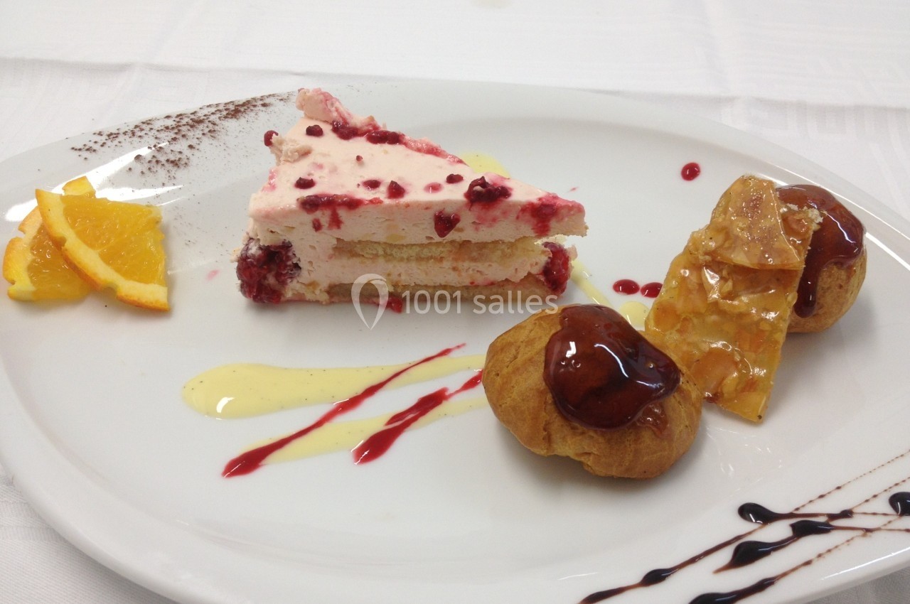 Assiette de dessert composée d'une part de gâteau aux fruits rouges, de choux garnis et de décorations sucrées.
