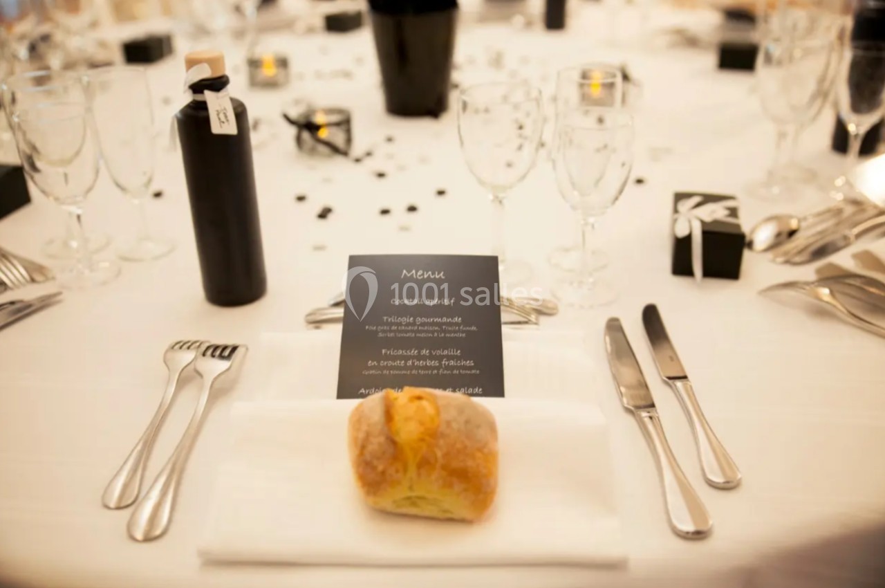 Table dressée avec élégance, comprenant couverts, verre, menu, pain individuel et décoration sobre.