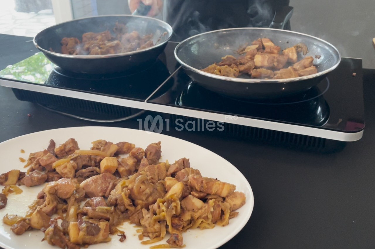 Morceaux de viande sautés avec des oignons dans deux poêles, servis sur une assiette blanche au premier plan.