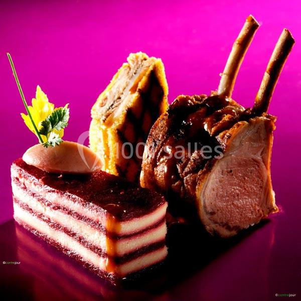 Assiette gastronomique avec carré d'agneau, millefeuille salé et gâteau à étages sur fond rose vif.
