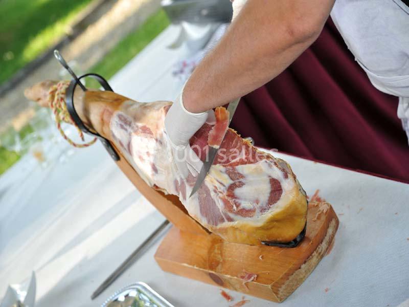 Traiteur Arsac (Gironde) - Domaine de Cordet #7 Une personne découpe finement un jambon entier posé sur un support en bois, en extérieur.