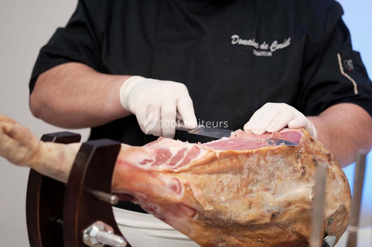 Traiteur Arsac (Gironde) - Domaine de Cordet #6 Un professionnel découpe finement un jambon cru sur un support en bois, portant des gants blancs.