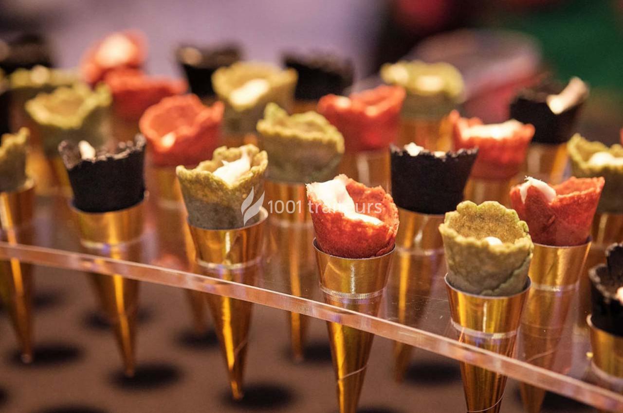 Cônes apéritifs colorés garnis de crème, disposés sur un présentoir transparent avec des supports dorés.