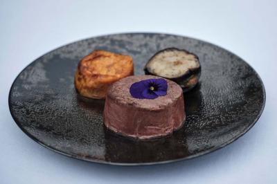 Un kiosque blanc au bord d'un étang avec une fontaine, entouré d'arbres et d'une réception en arrière-plan.