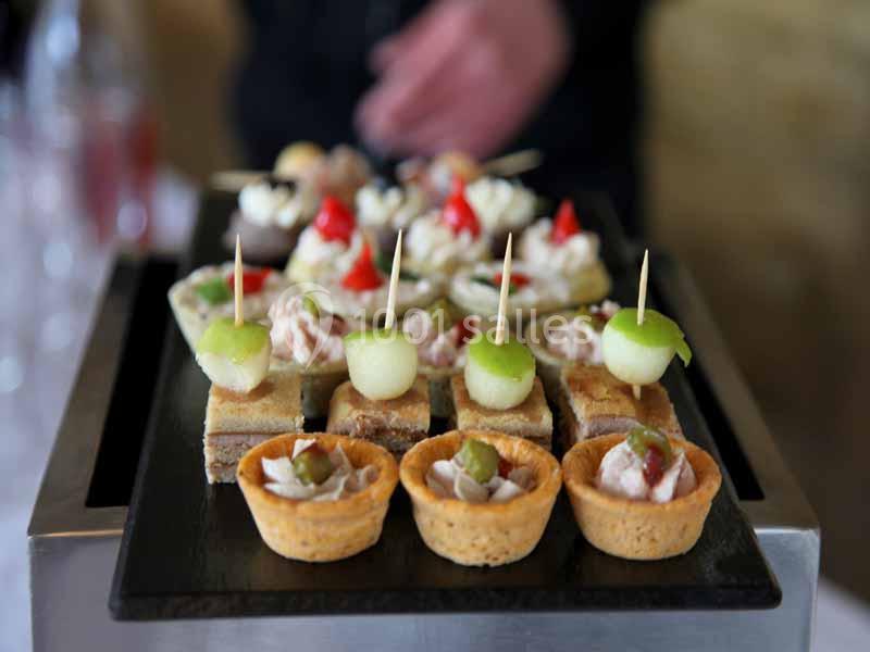 Plateau de bouchées apéritives variées, comprenant des tartelettes, des brochettes de melon et des toasts garnis.