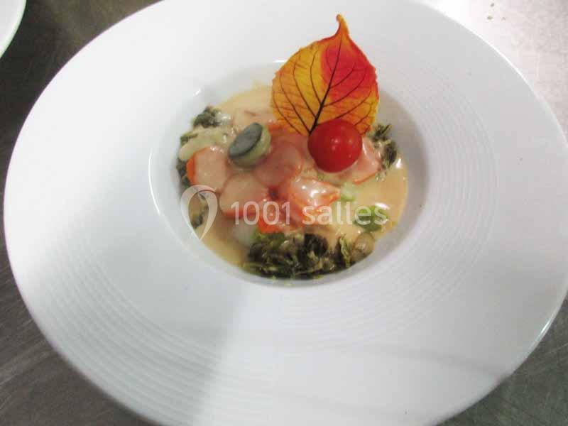 Assiette contenant des légumes, une sauce crémeuse et une décoration avec une feuille colorée et une tomate cerise.