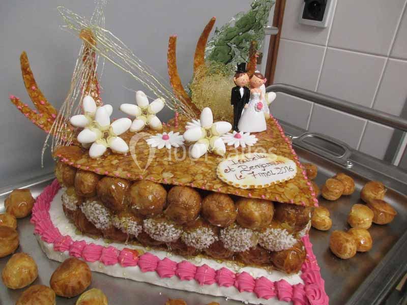 Pièce montée en choux décorée de fleurs en sucre, d'amandes et de figurines de mariés, posée sur un plateau.
