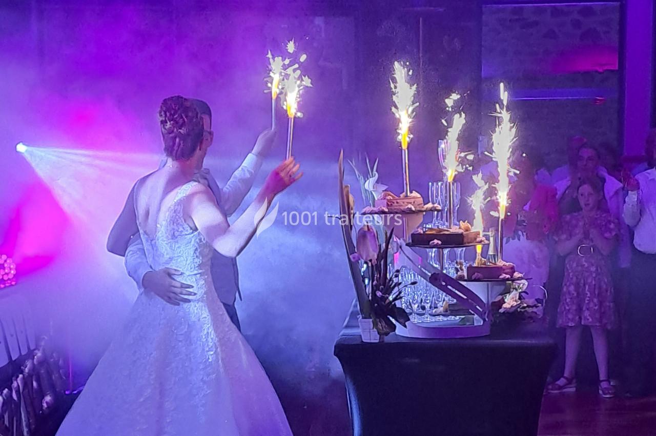 Un couple en tenue de mariage tient des cierges magiques près d'une table de desserts, entouré de fumée et de lumière.