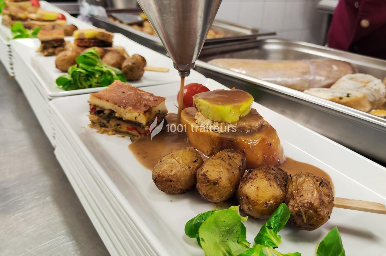 Assiette gastronomique avec viande en sauce, pommes de terre rôties, légumes et garniture, en cours de dressage.