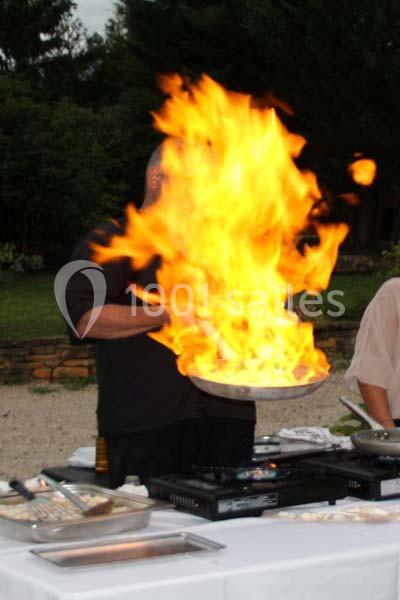 Un cuisinier manipule une poêle avec une flamme vive lors d'une démonstration en extérieur.