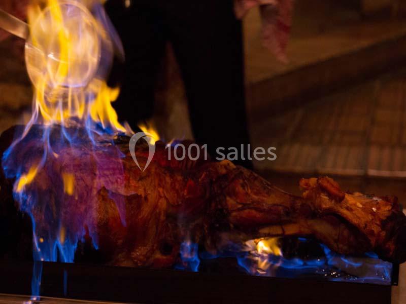 Un plat de viande en train de flamber avec des flammes bleues dans un environnement sombre.