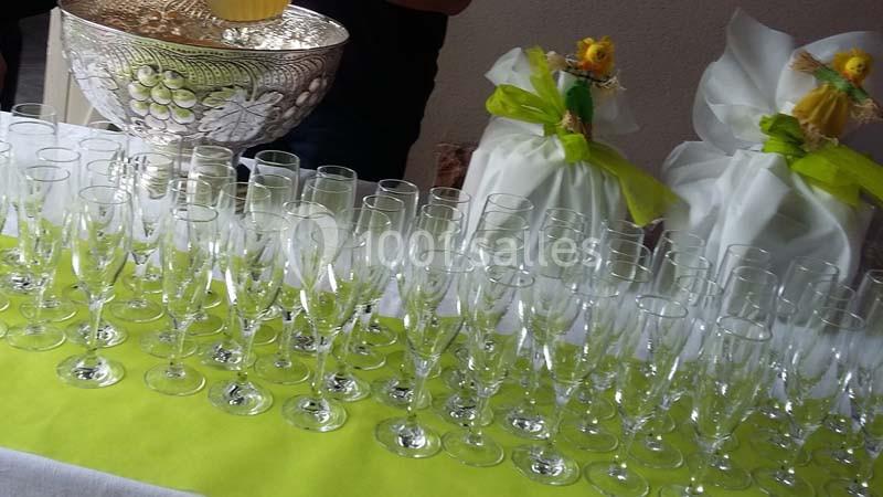 Rangée de verres à pied alignés sur une nappe verte, avec des décorations florales en arrière-plan.