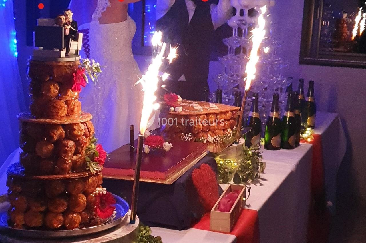 Pièce montée en choux et gâteau entourés de décorations festives, avec des bouteilles de champagne en arrière-plan.