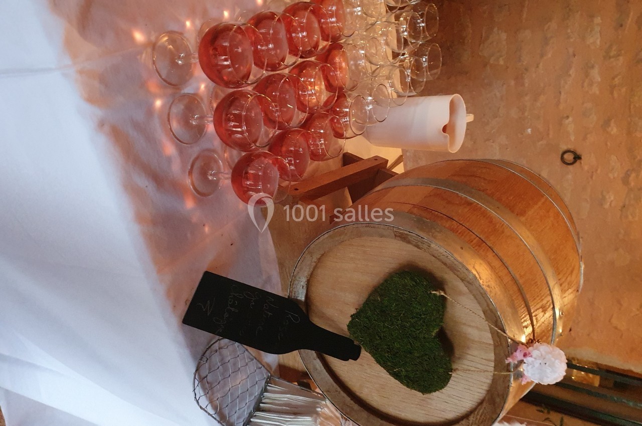 Table décorée avec des verres de cocktail rose, un tonneau en bois orné de mousse en forme de cœur et une bougie.