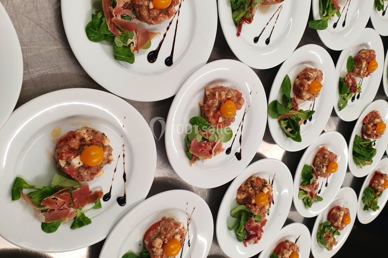 Assiettes dressées avec tartare, tomates cerises, roquette, jambon cru et filet de vinaigre balsamique.