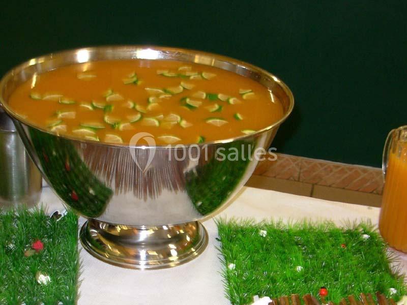 Grande coupe en métal remplie de punch orange avec des tranches de citron vert, posée sur une table décorée.