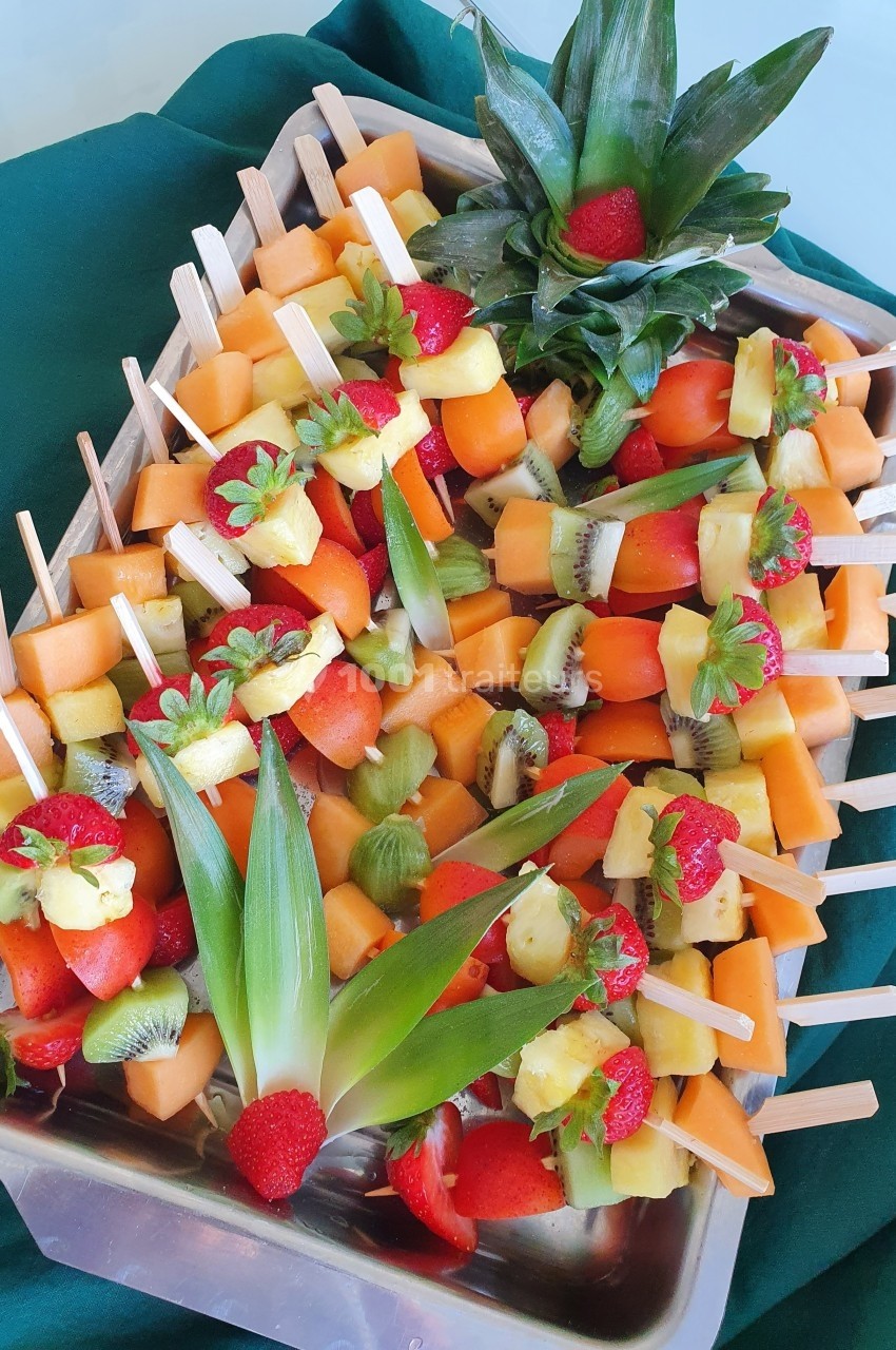 Brochettes de fruits frais variés, disposées sur un plateau avec des décorations d'ananas et de fraises.