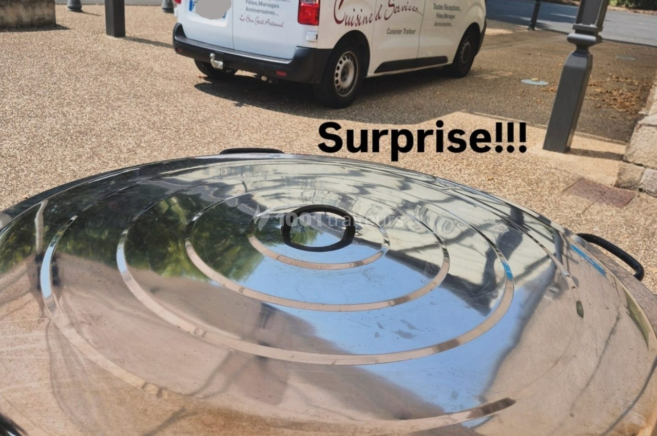 Vue d'un couvercle métallique brillant au premier plan avec une camionnette de traiteur stationnée en arrière-plan.