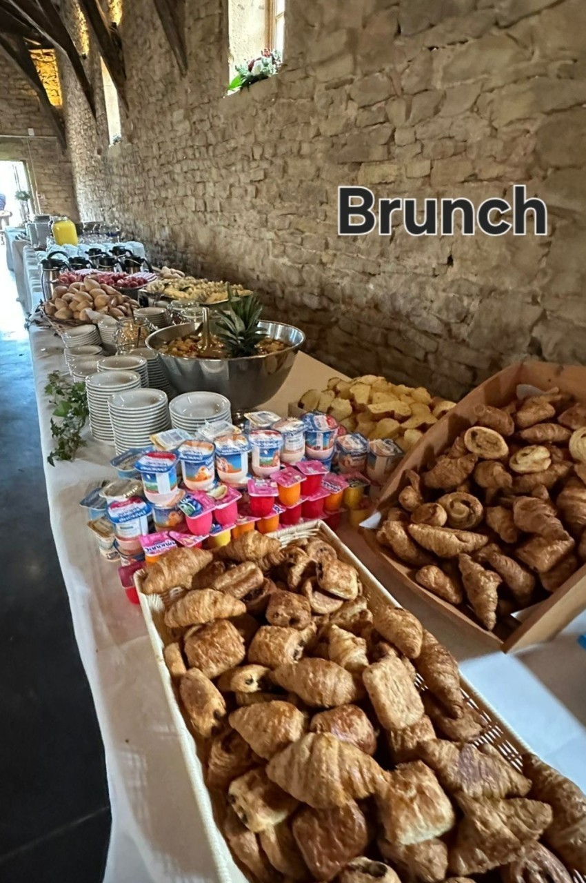 Buffet de brunch avec viennoiseries, yaourts, fruits et autres plats disposés sur une longue table en pierre.