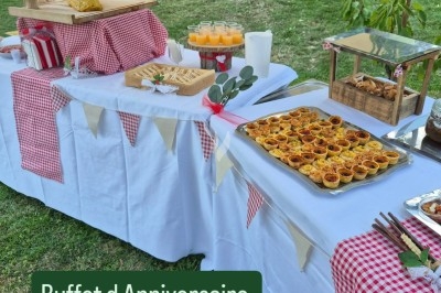 Buffet d'anniversaire en extérieur avec nappes blanches, plats variés, boissons et décor champêtre.