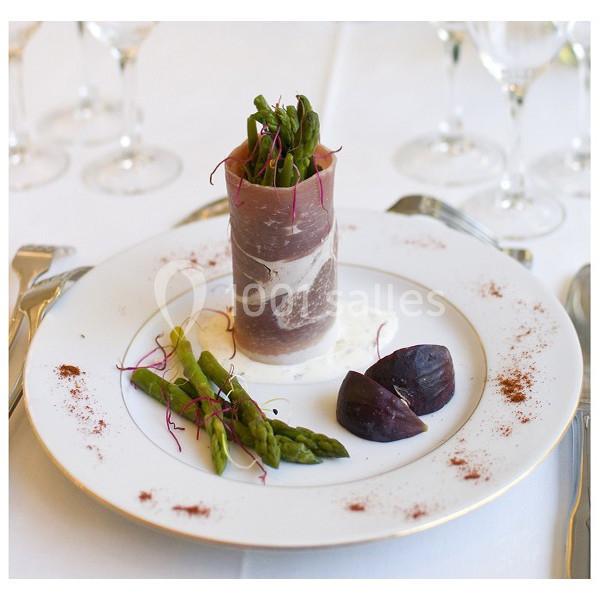 Assiette gastronomique avec roulé de viande, asperges, betteraves et sauce, présentée sur une table dressée.