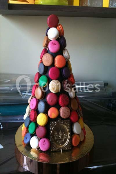 Pyramide de macarons colorés disposés sur un support conique, posée sur une base dorée.