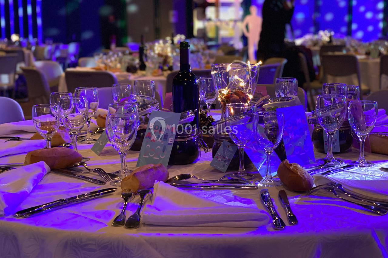 Table dressée pour un dîner festif avec nappes blanches, verres, couverts, bougies et décorations lumineuses.