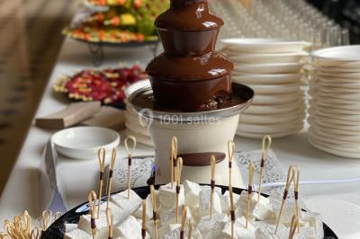 Miniature Traiteur Arnouville-lès-Mantes (Yvelines) - MBRA Traiteur #28 Fontaine à chocolat sur une table de buffet avec des fruits frais et des brochettes en arrière-plan.