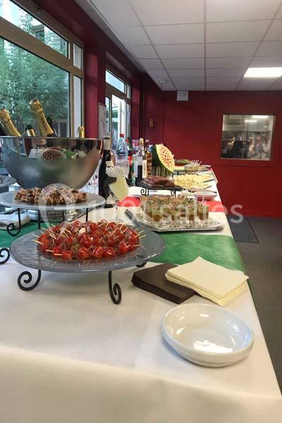 Buffet avec verrines, brochettes et boissons disposés sur une table blanche dans une salle lumineuse.