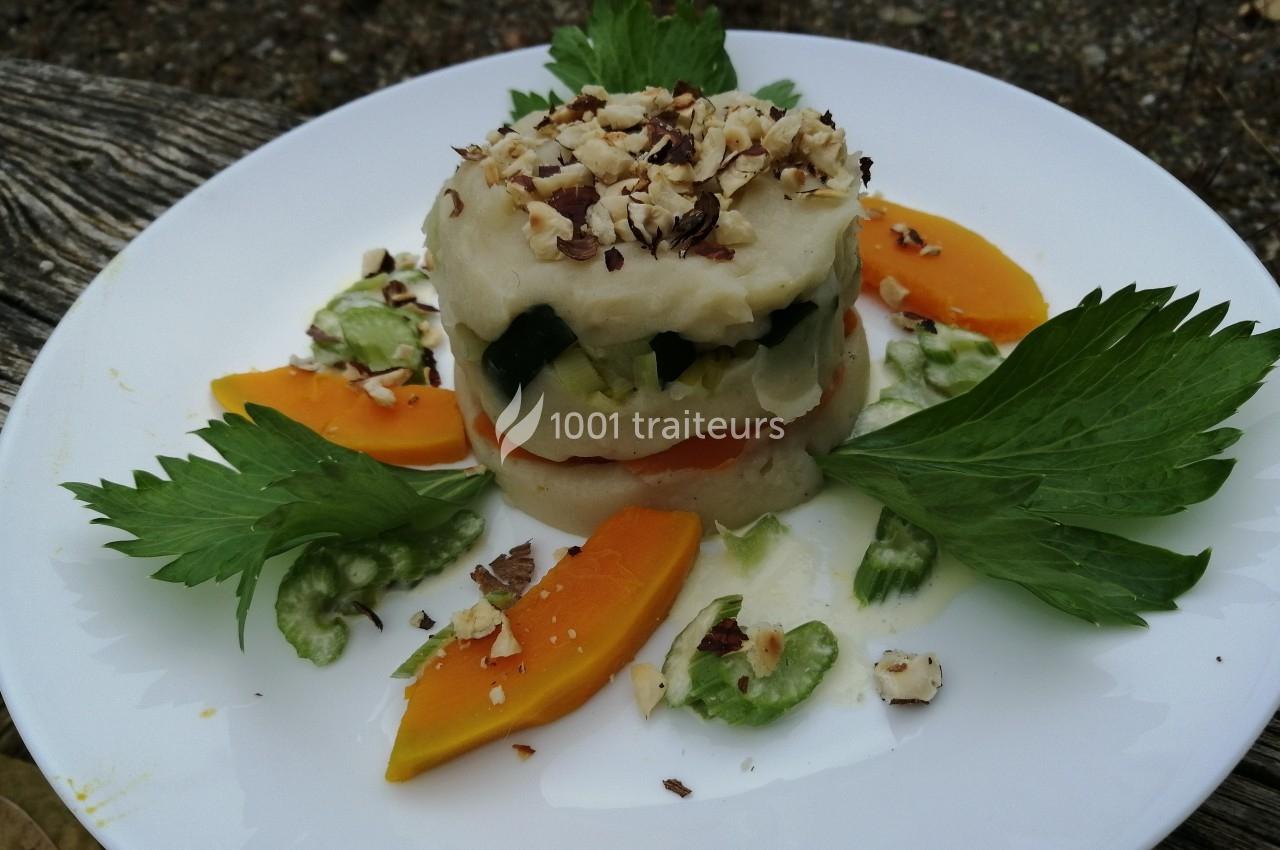 Assiette de légumes colorés avec purée, courgettes, carottes, céleri et éclats de noisettes, présentée sur une table en bois.