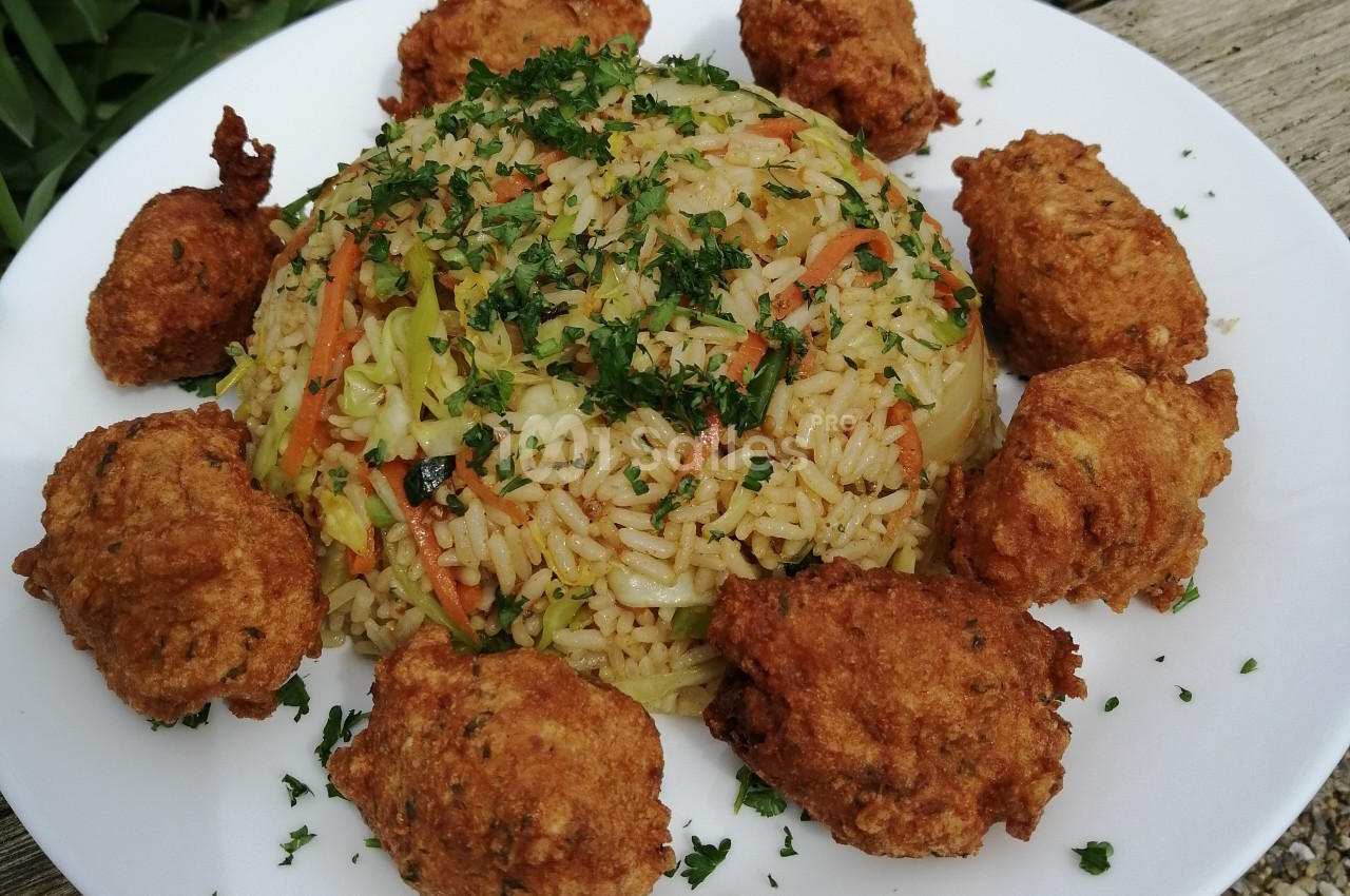 Assiette de riz sauté aux légumes garnie de beignets dorés et parsemée de persil haché.