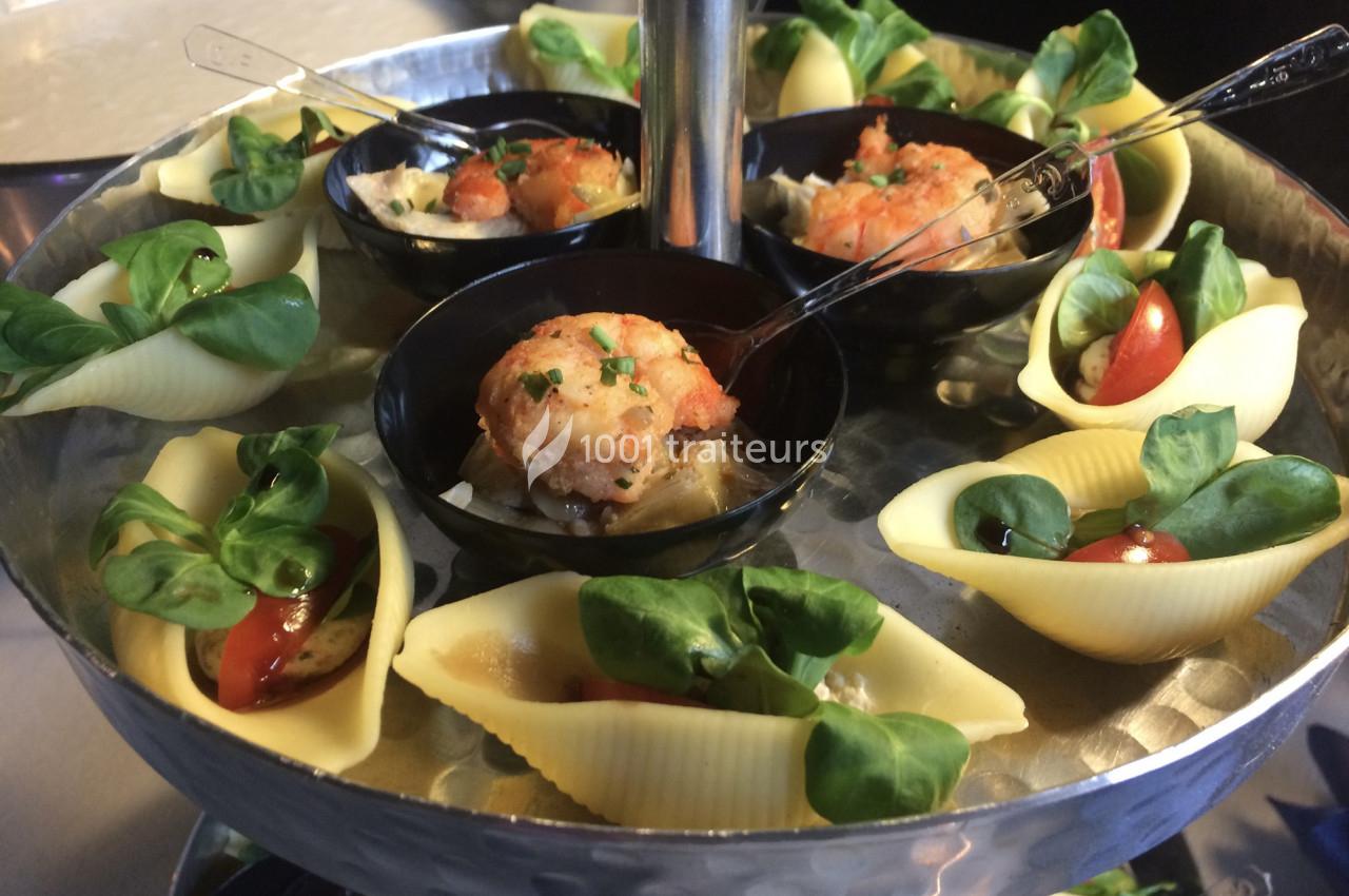 Plateau de présentation avec des coquilles de pâtes garnies de mâche, tomates cerises et verrines de crevettes.