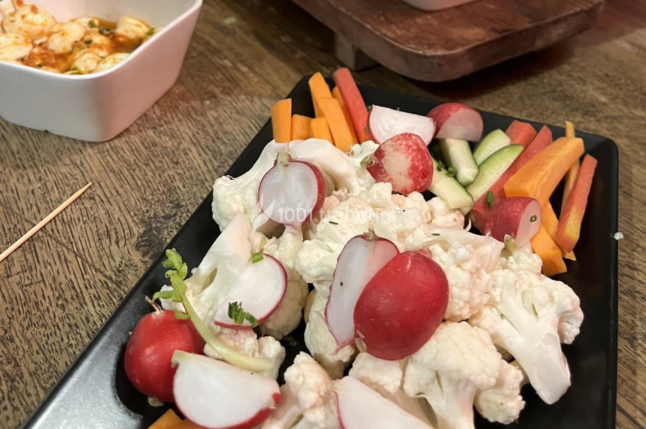Assiette de crudités composée de radis, chou-fleur, carottes et concombres, servie sur une table en bois.