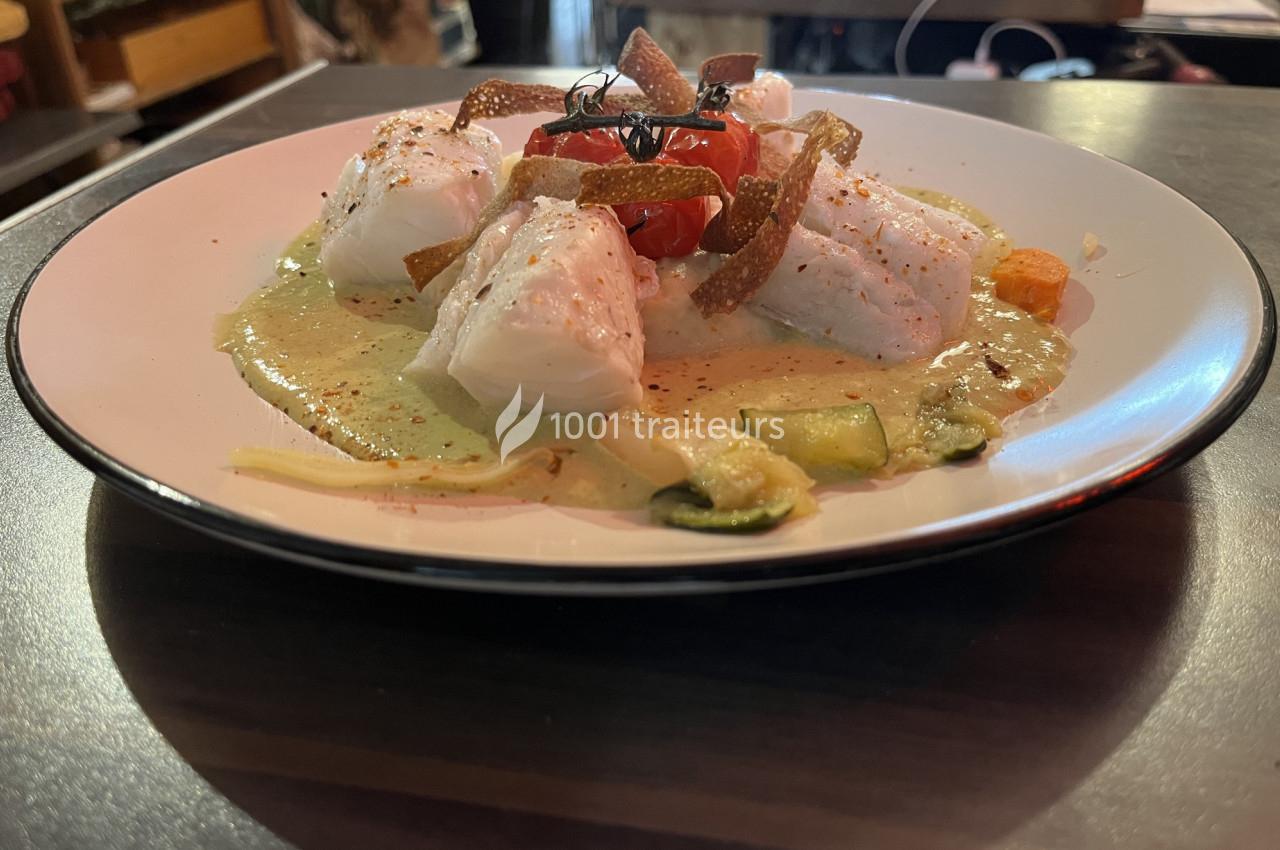 Assiette de poisson blanc avec sauce crémeuse, légumes sautés et chips croustillantes, servie sur une table en bois.