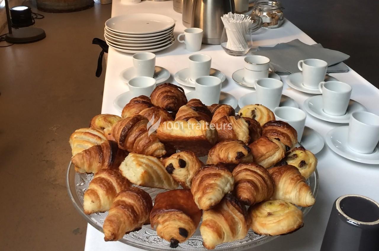 Plateau de viennoiseries variées sur une table dressée avec des tasses, des assiettes et des accessoires pour le café.