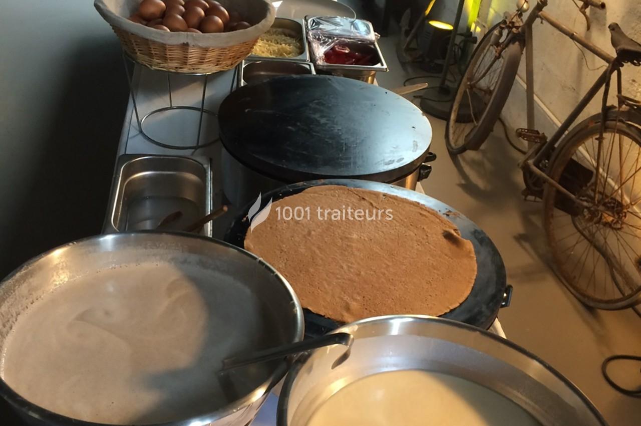 Préparation de crêpes sur des plaques chauffantes avec des ingrédients disposés sur une table à proximité.
