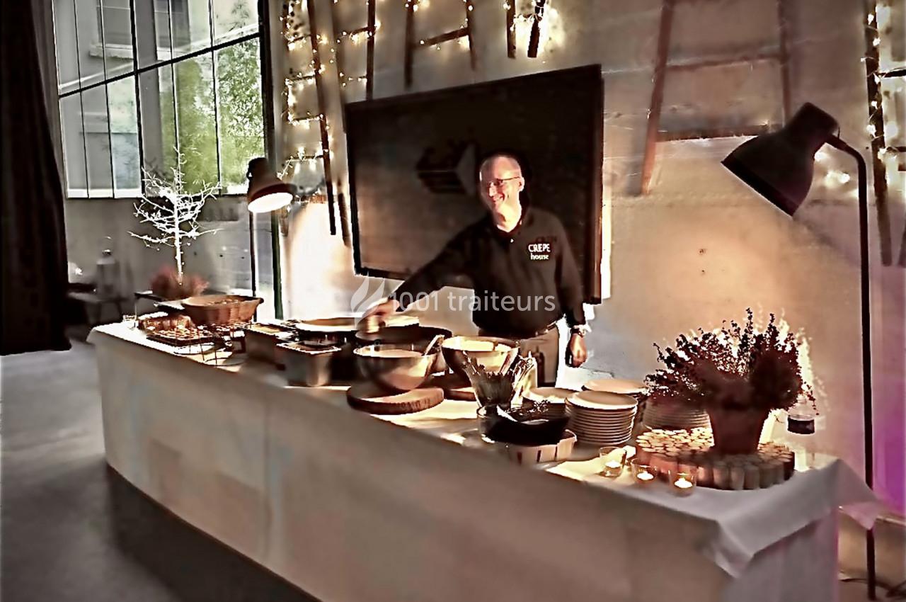 Un chef présente un buffet avec des plats variés, disposés sur une table éclairée dans un espace moderne et chaleureux.