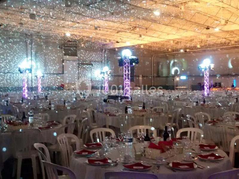 Salle de réception décorée avec des tables dressées, des nappes blanches et des éclairages lumineux colorés.