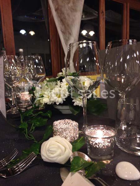 Table élégamment dressée avec fleurs blanches, bougies allumées et verres à pied dans un cadre intérieur.