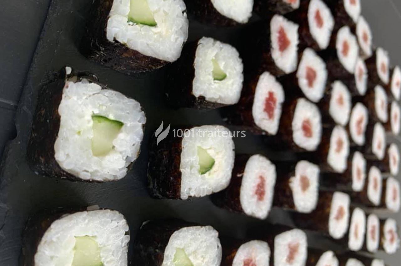 Plateau de makis alignés, garnis de concombre ou de poisson cru, sur une surface noire.
