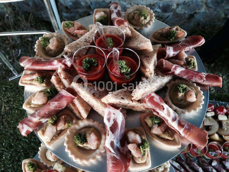 Assortiment d'amuse-bouches avec jambon, crevettes en tartelettes et verrines de sauce rouge sur un plateau.