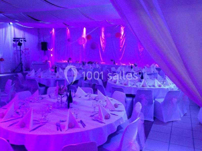 Salle de réception décorée avec des tables rondes dressées, éclairage violet et ambiance festive.