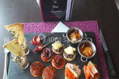 Plateau de mini-burgers, bouchées variées et garnitures sur une ardoise noire, présenté sur une nappe sombre.