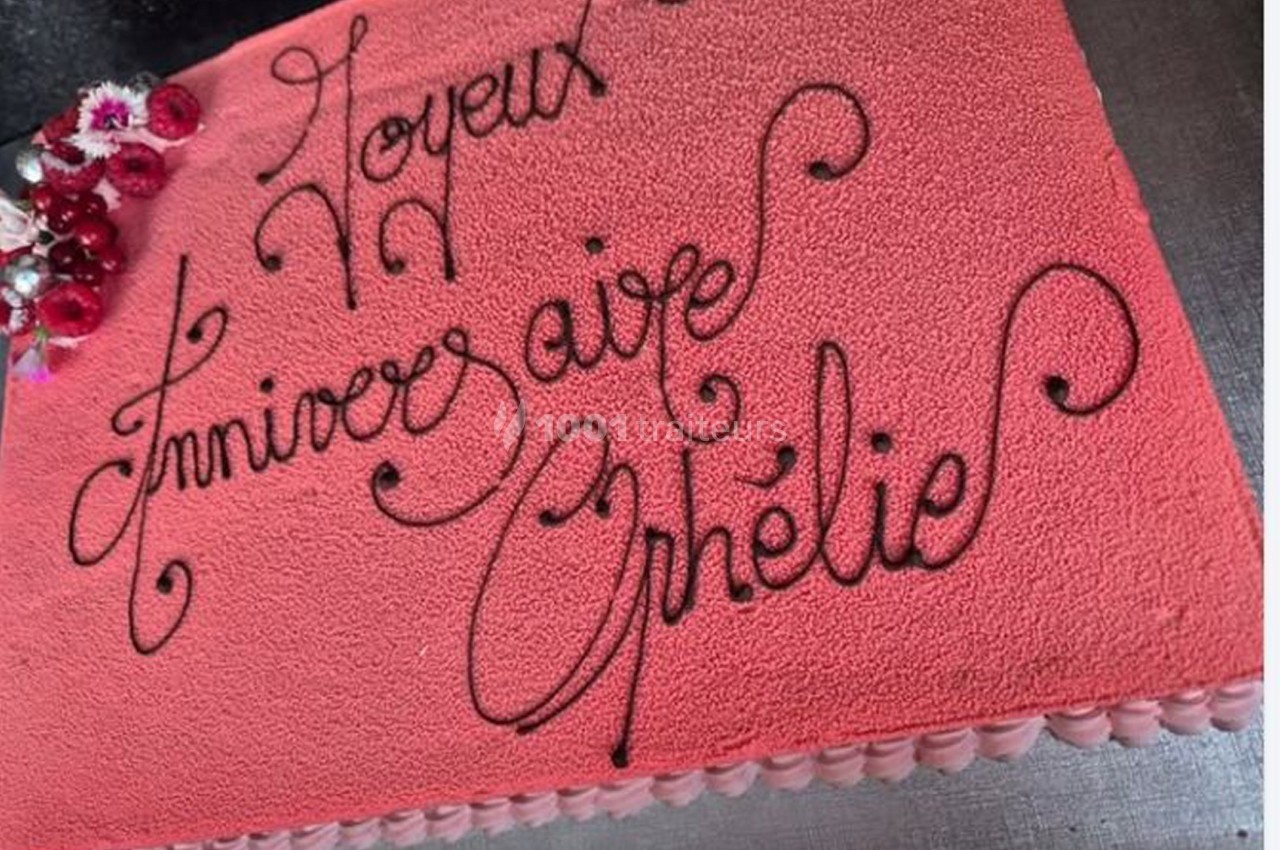 Gâteau d'anniversaire rose avec un message écrit en chocolat et des fleurs décoratives dans un coin.