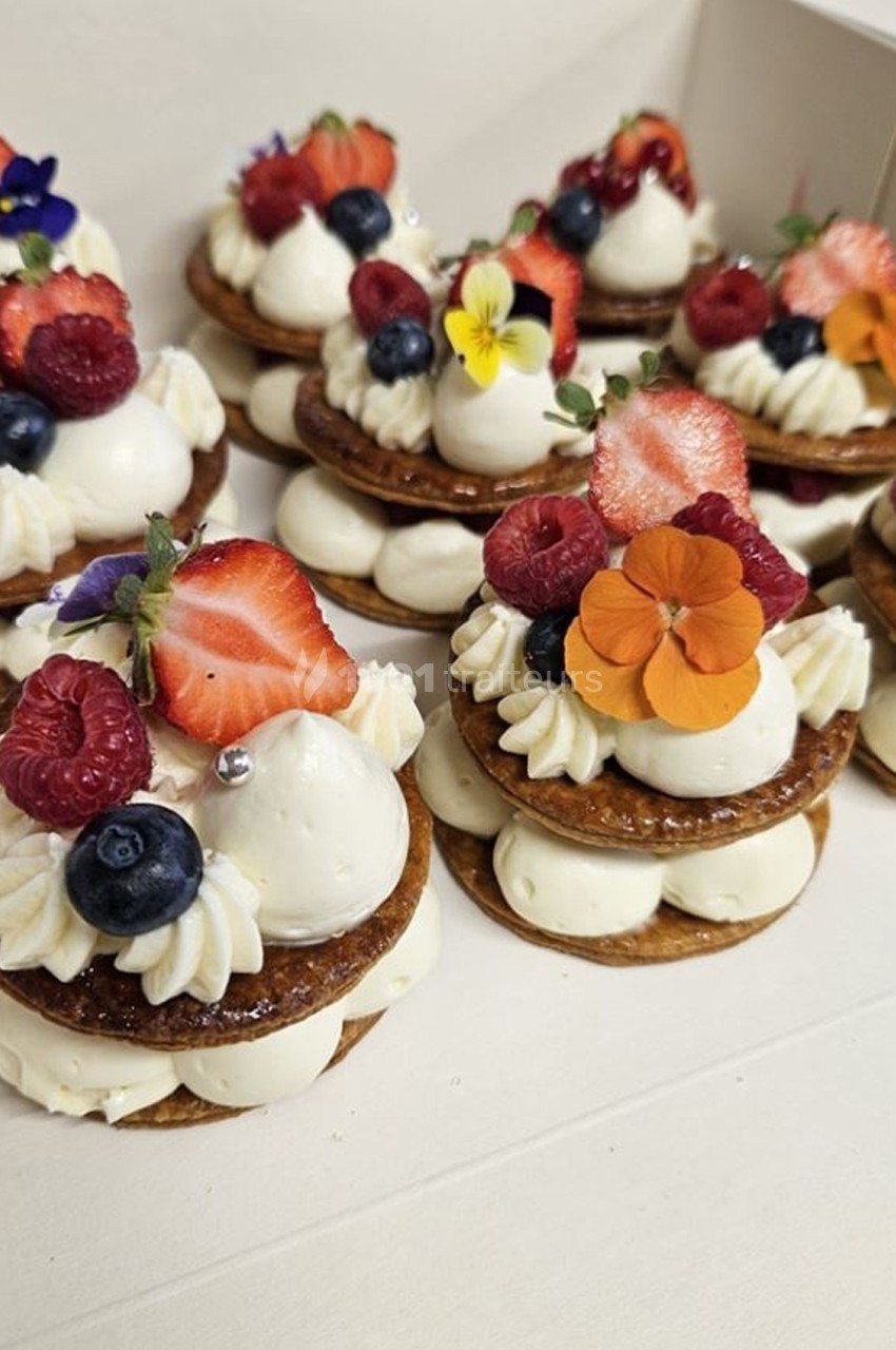 Desserts individuels composés de disques de pâte, crème blanche, fruits rouges et fleurs comestibles colorées.