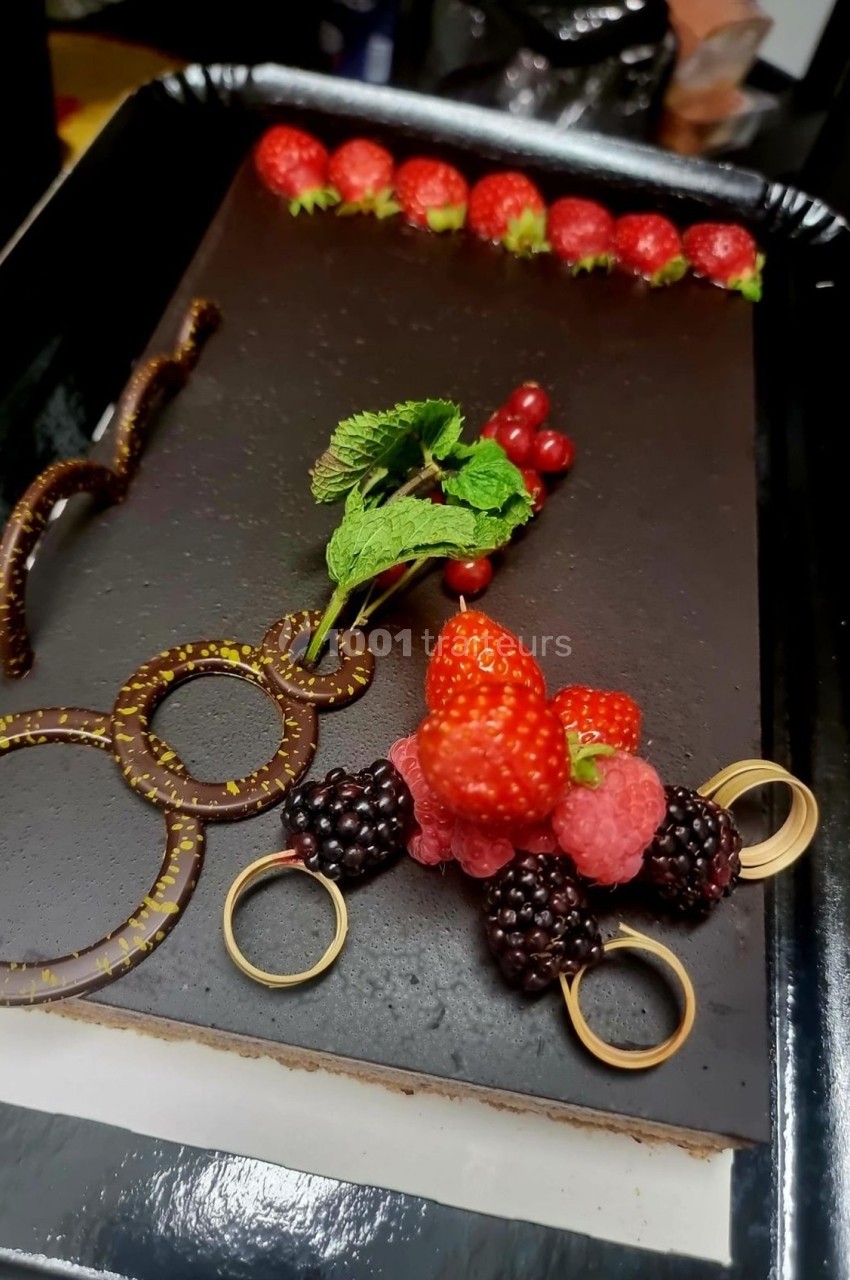 Gâteau au glaçage chocolat, décoré de fruits rouges, mûres, framboises, menthe et éléments en chocolat.