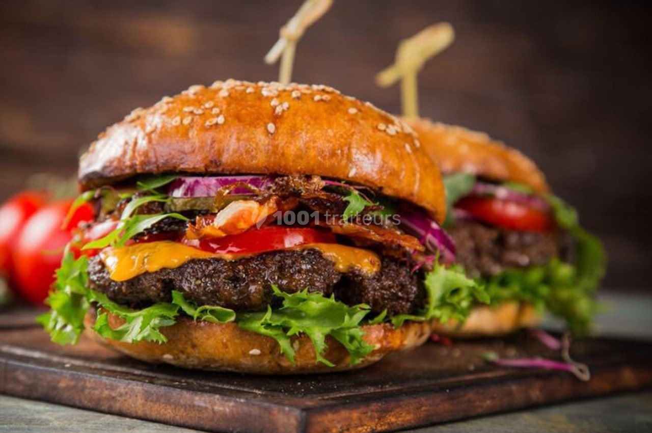 Deux burgers garnis de viande, fromage, salade, tomates et oignons, servis sur une planche en bois.