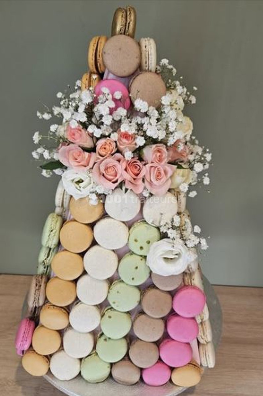 Pyramide de macarons colorés décorée de roses roses et de fleurs blanches sur une table en bois.